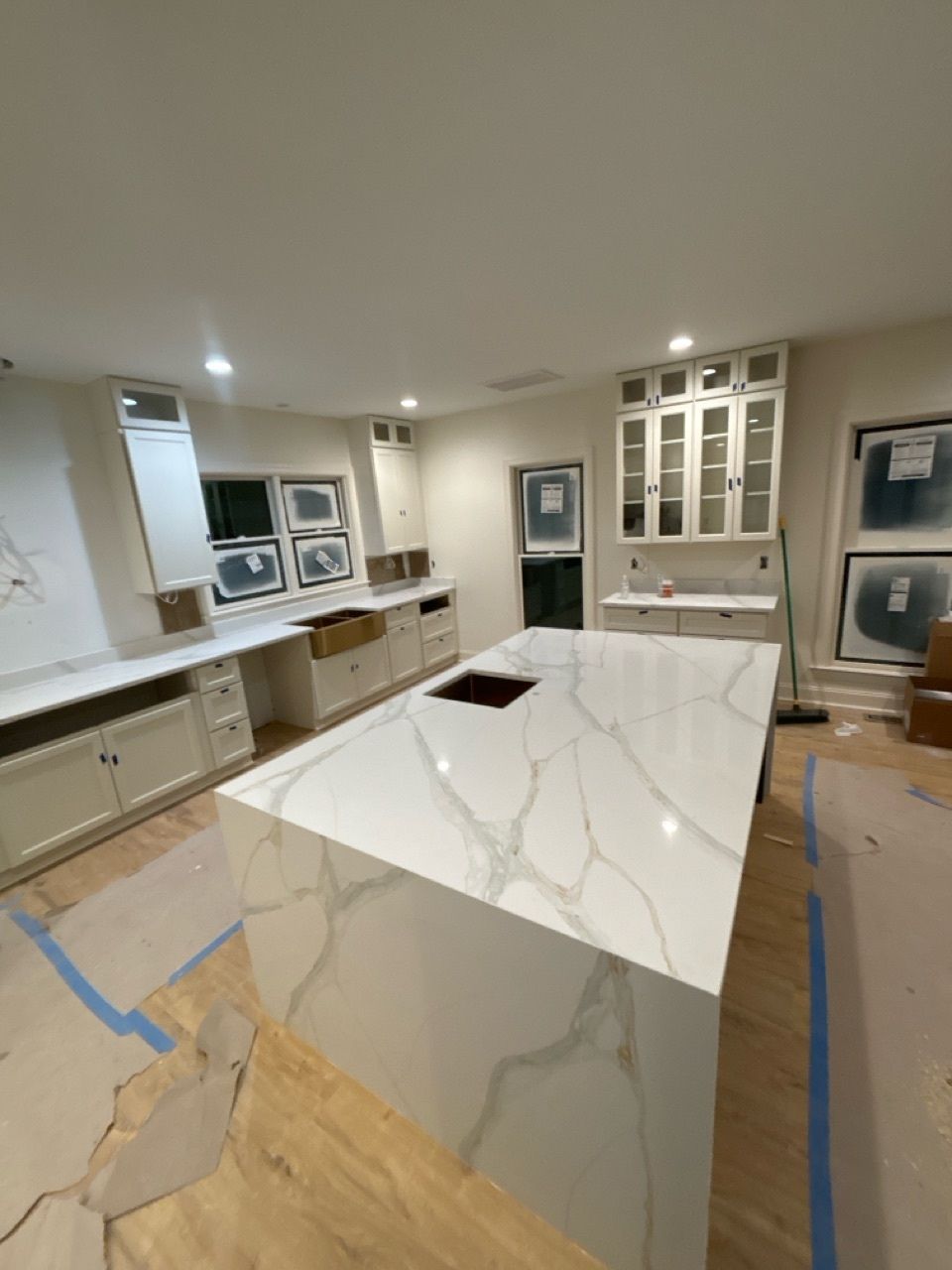 Kitchen renovation: white countertops and cabinets, large island with cooktop, light wood floor, open windows.