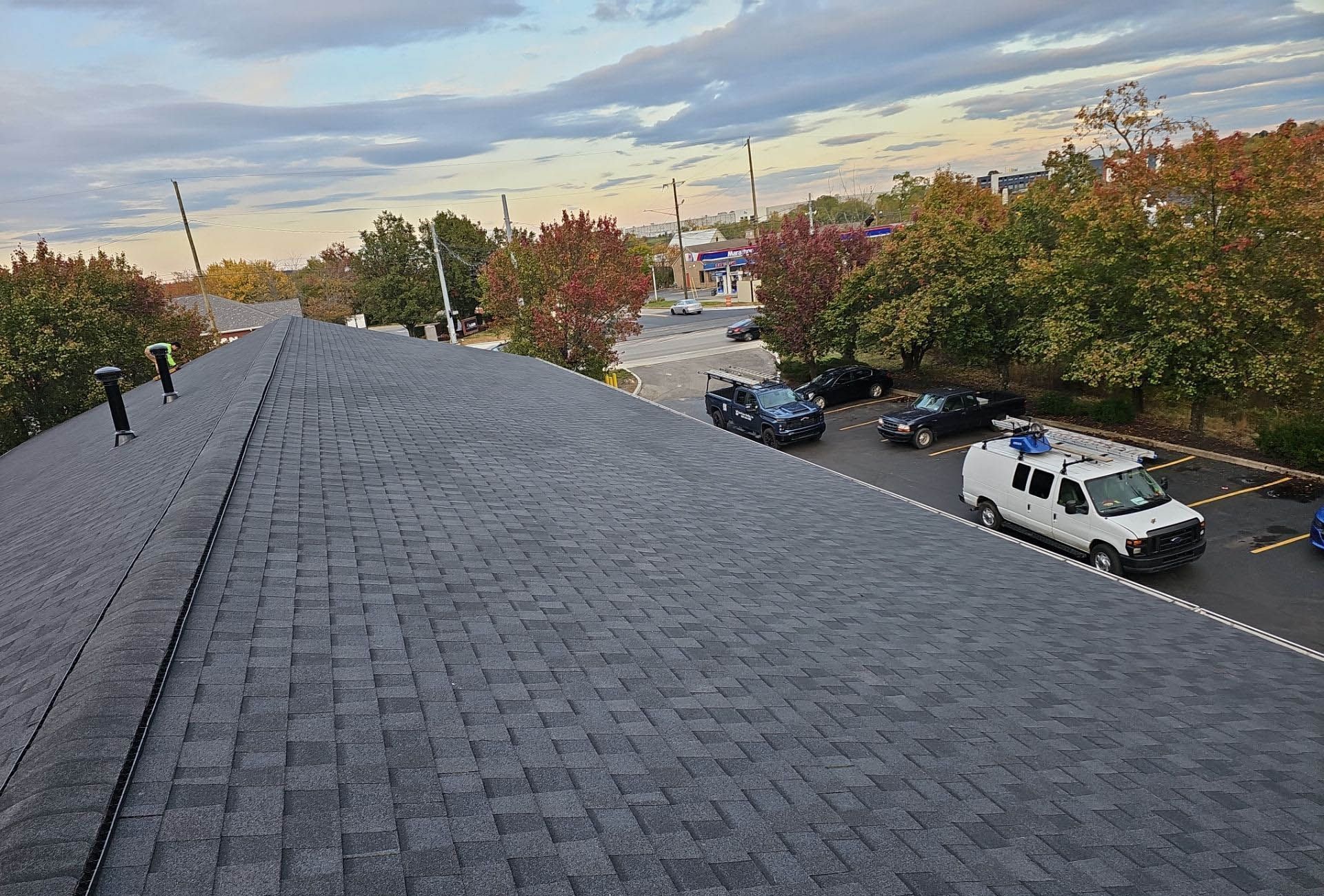Gray asphalt shingle roof, overlooking a street with police vehicles and trees in autumn colors under a cloudy sky.