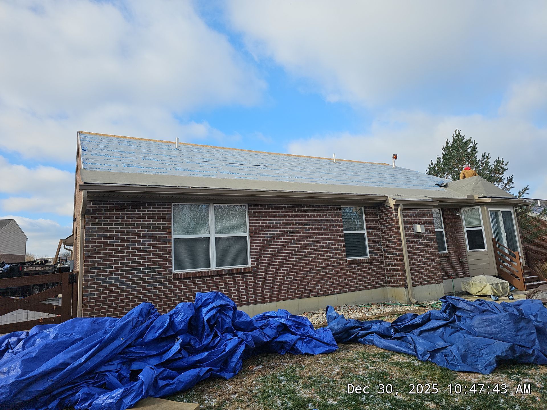 A brick house with a partially replaced roof; blue tarps lie on the ground.