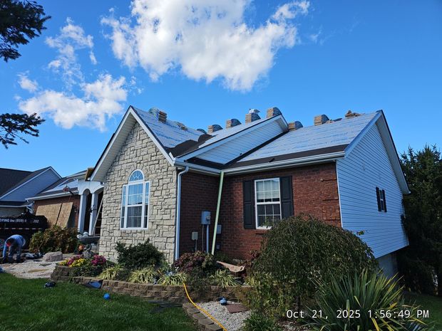 House with a metal roof under construction; blue sky, brick, and stone facade visible.