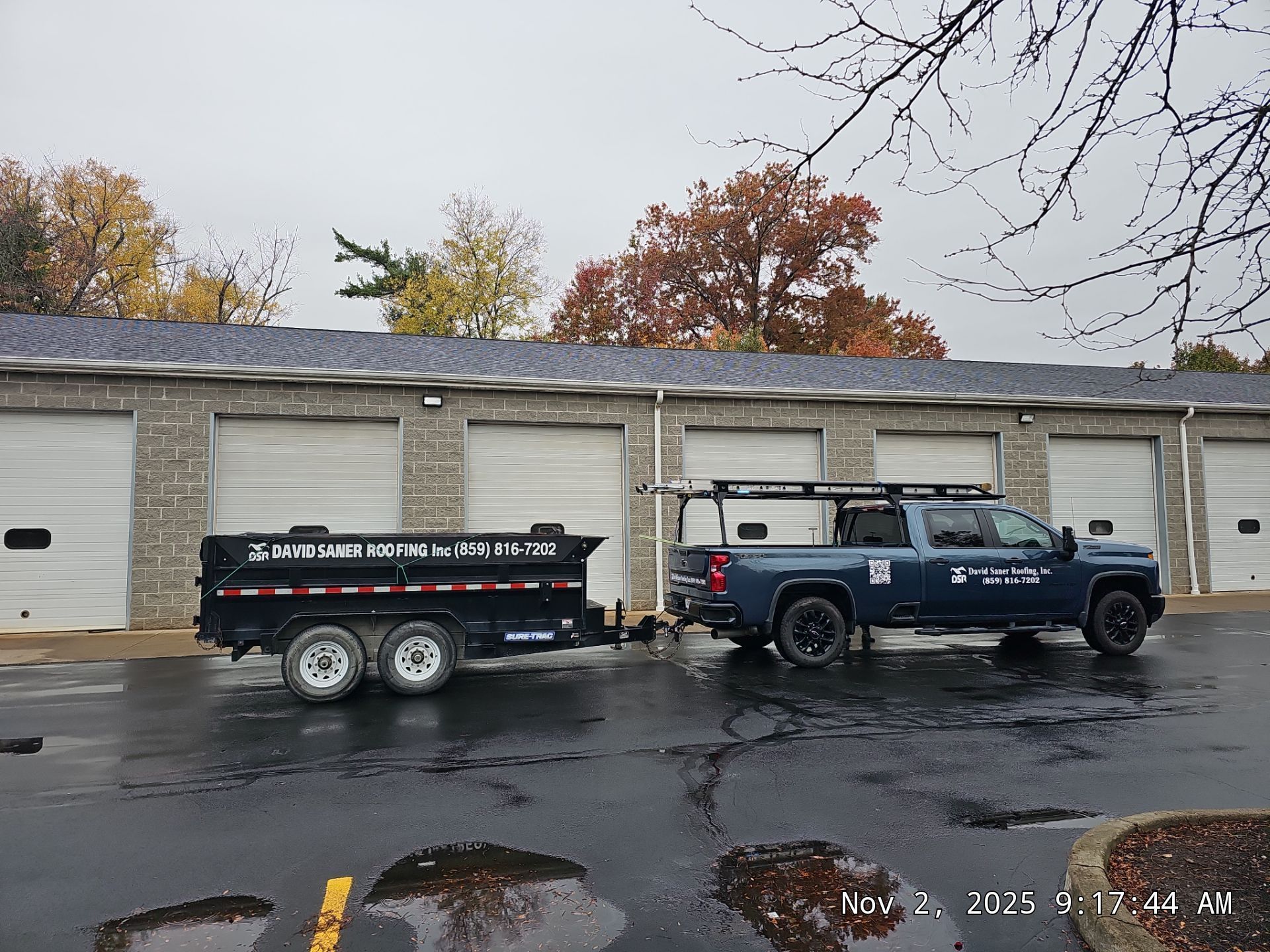 Truck pulling a trailer in front of a building with garage doors. The truck and trailer are blue and black.