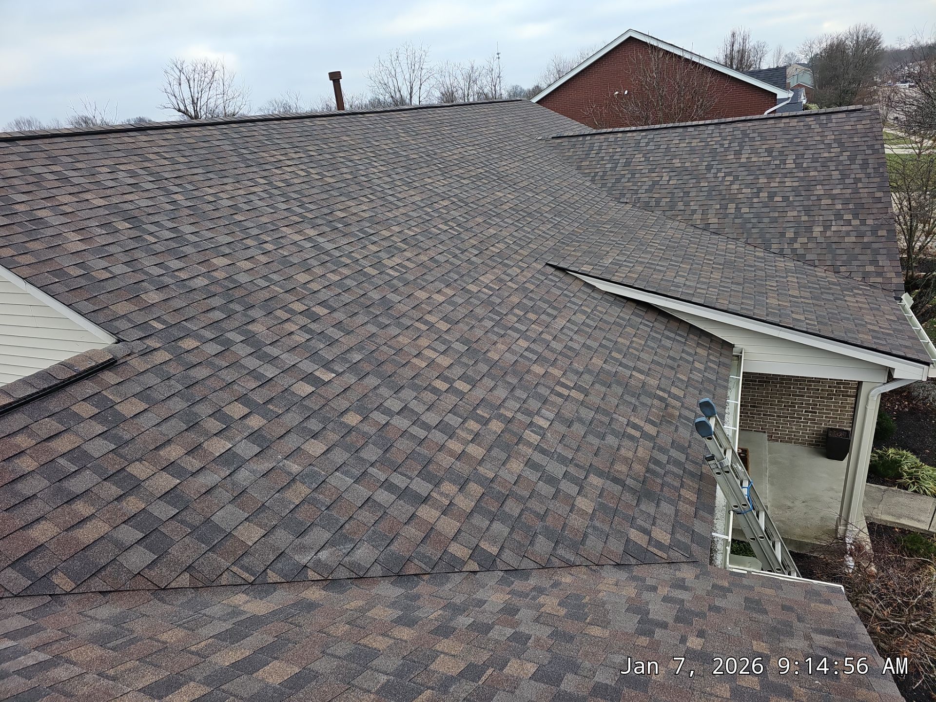 Newly shingled residential roof with brown and tan shingles, under a cloudy sky.