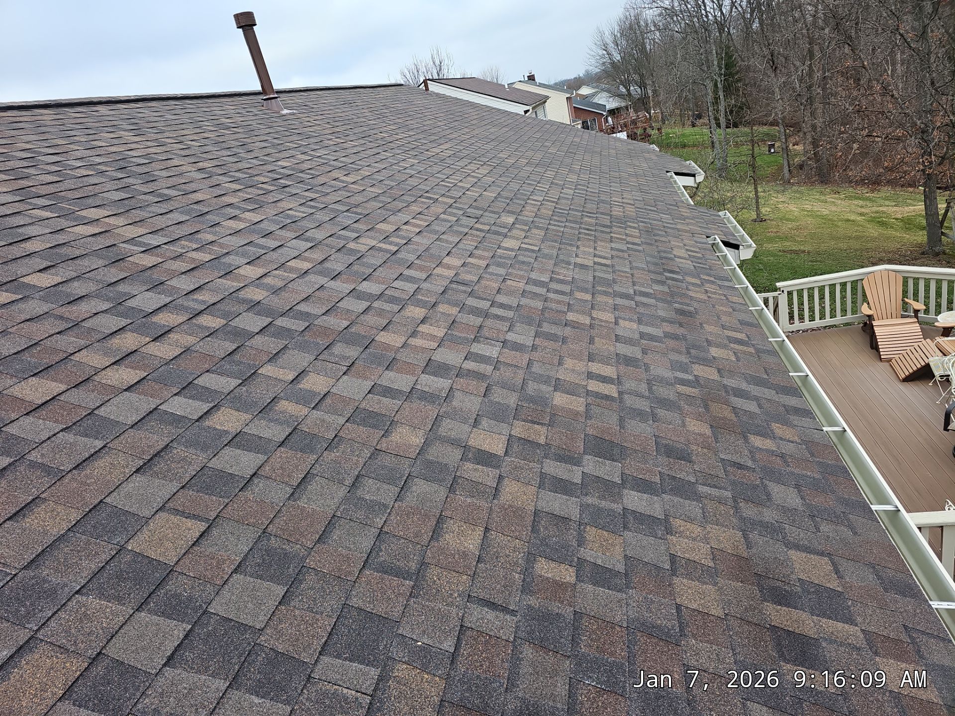 View of a brown and black asphalt shingle roof, with a gutter and a deck on the side.