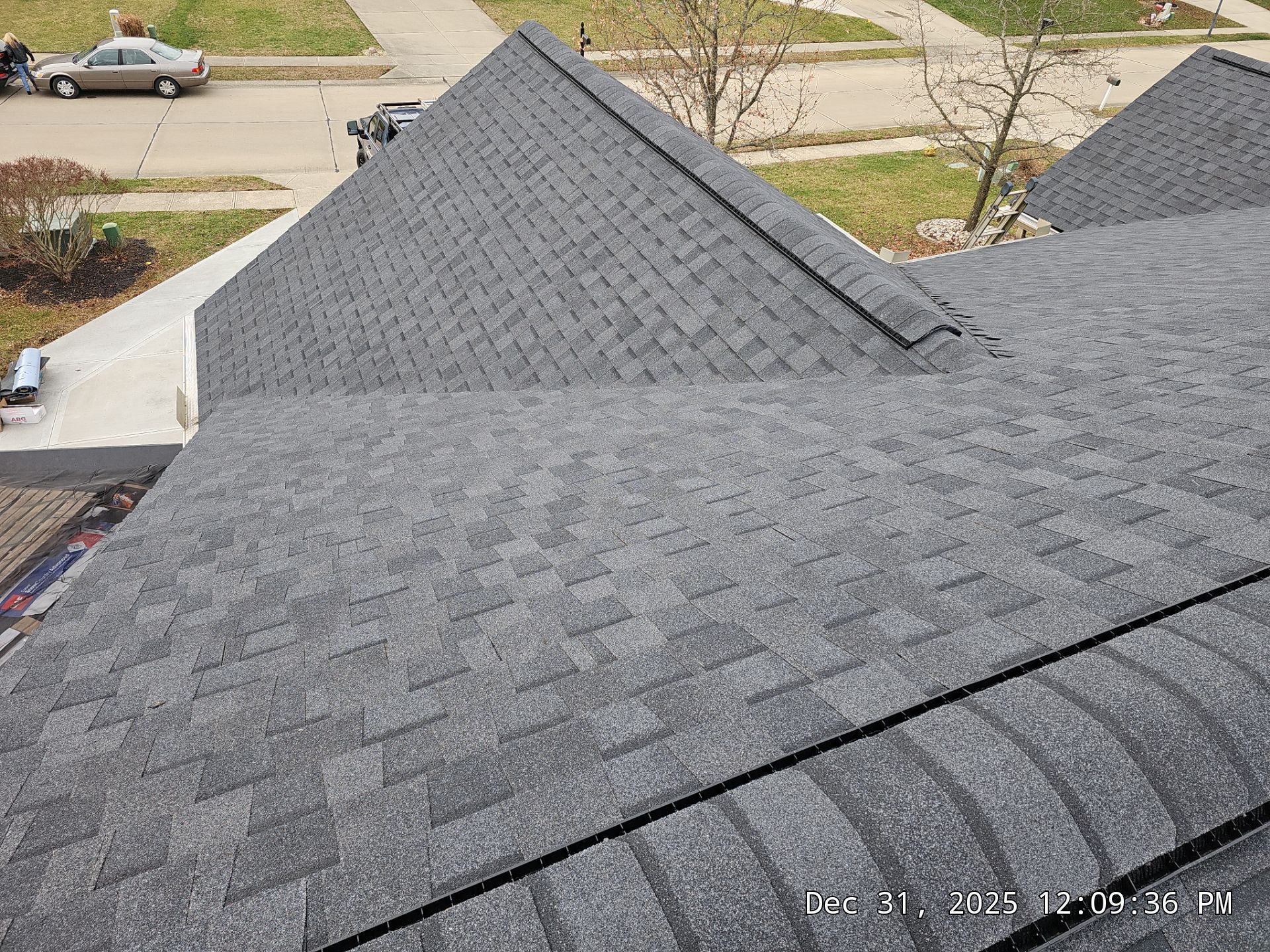 Grey asphalt shingle roof on a house, angled view of various roof sections and the neighborhood.