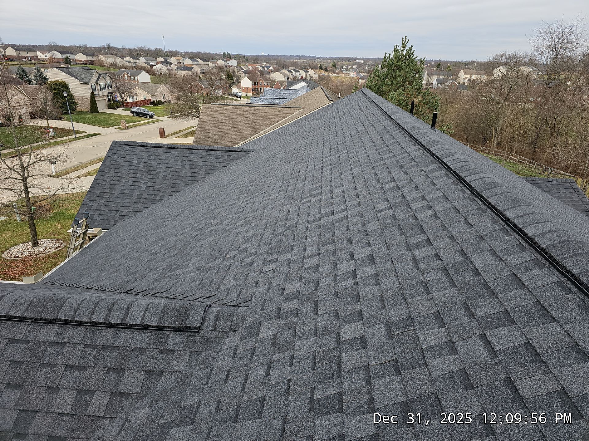 Dark gray asphalt shingle roof on a house, overlooking a suburban neighborhood.
