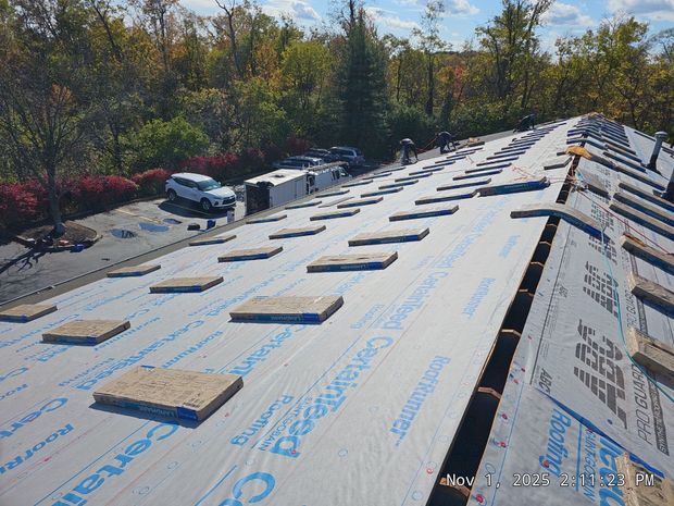 Rooftop construction: layers of underlayment, wooden blocks, and materials, with cars parked nearby.