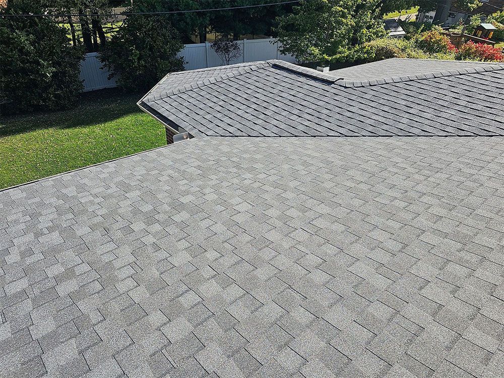 Overhead view of a gray asphalt shingle roof on a house, with green grass and white fence in the background.