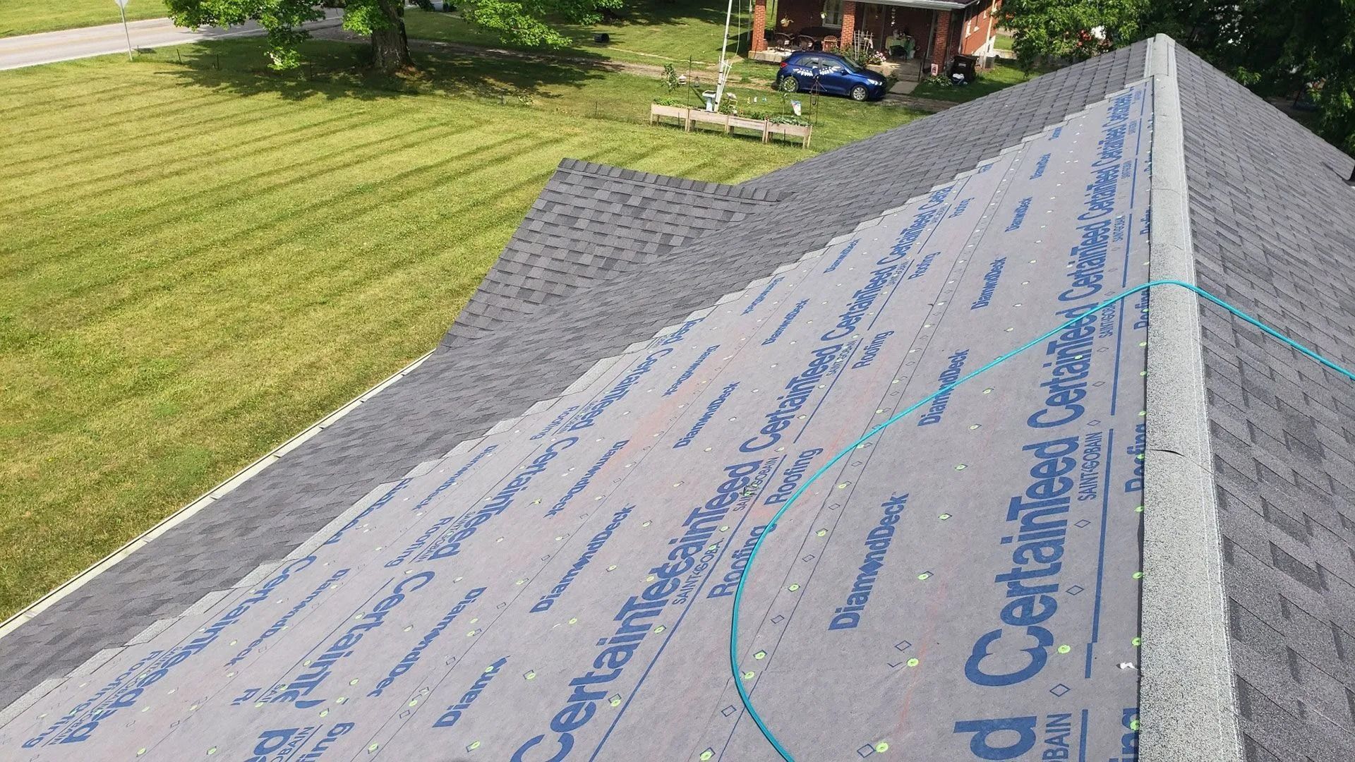 Overhead view of a roof in progress, with dark shingles and partially covered in a CertainTeed underlayment.
