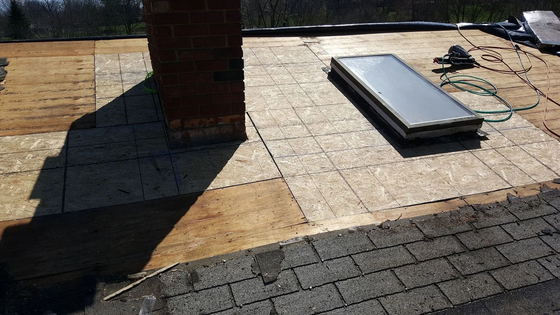 Roof with chimney and skylight, OSB sheathing visible, surrounded by asphalt shingles.