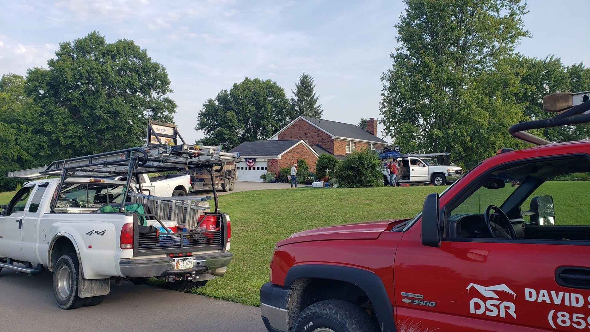 Several work trucks parked in front of a brick house. Workers are present on the lawn.