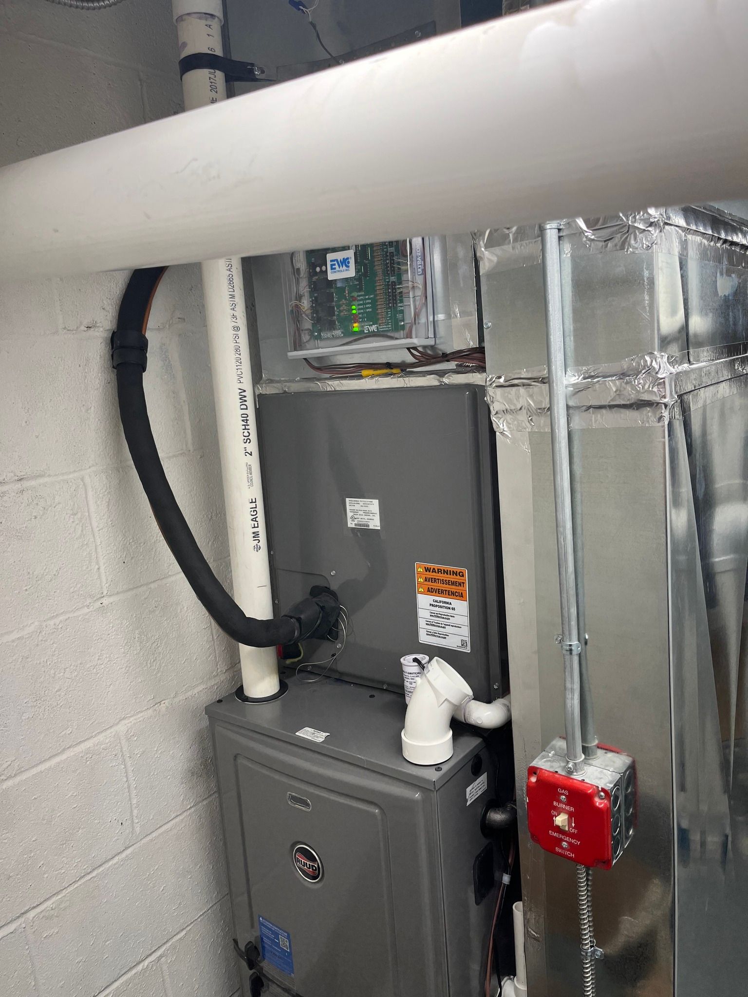 Furnace and air handler system in a utility room with ductwork, pipes, and a control panel.