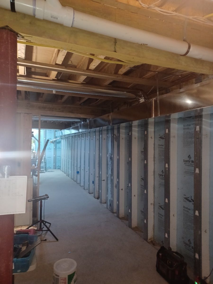 Basement under construction; unfinished walls, exposed beams, pipes. Light gray walls, concrete floor.