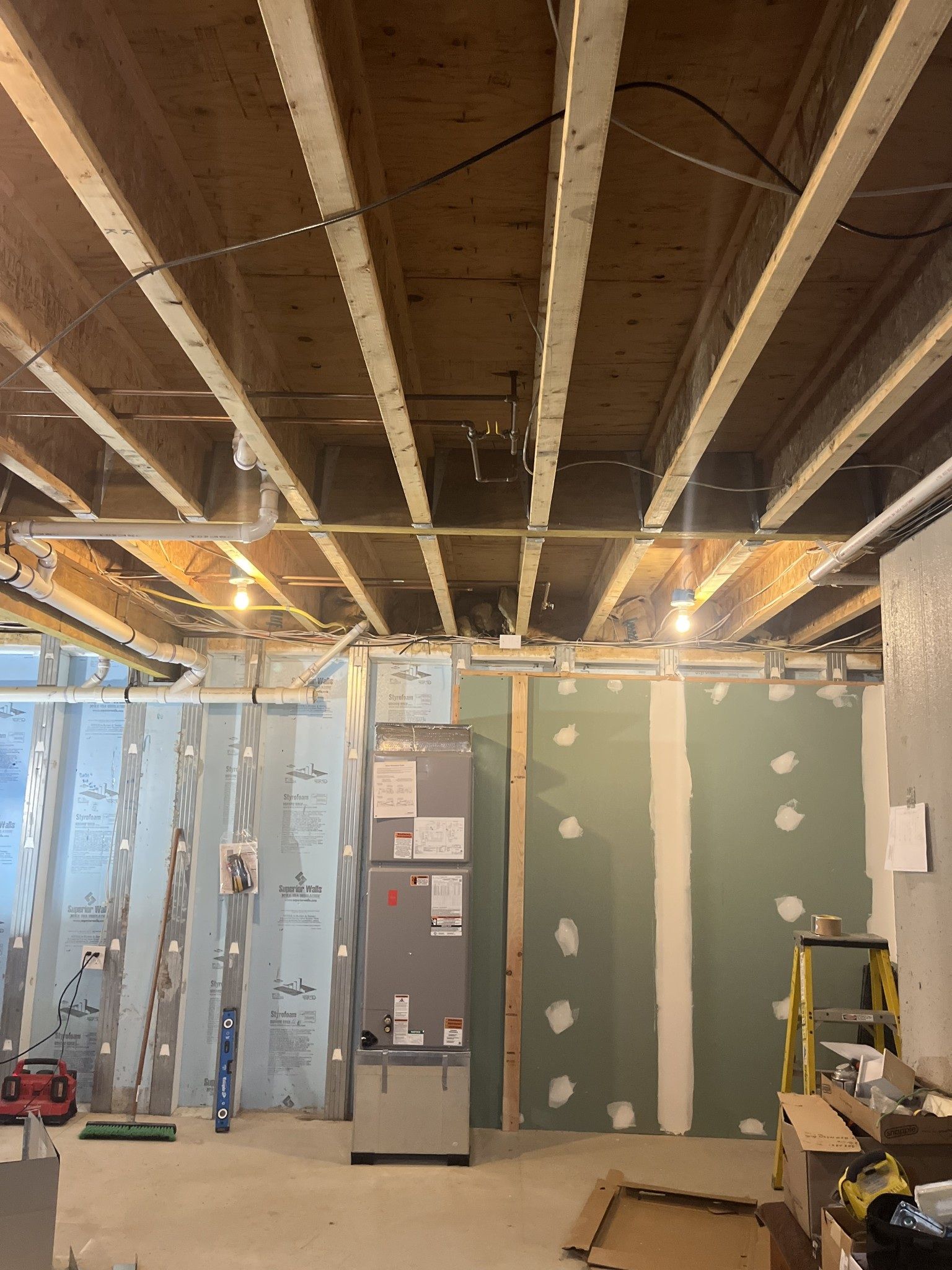 Basement under construction with exposed ceiling beams, insulation, HVAC unit, and drywall.