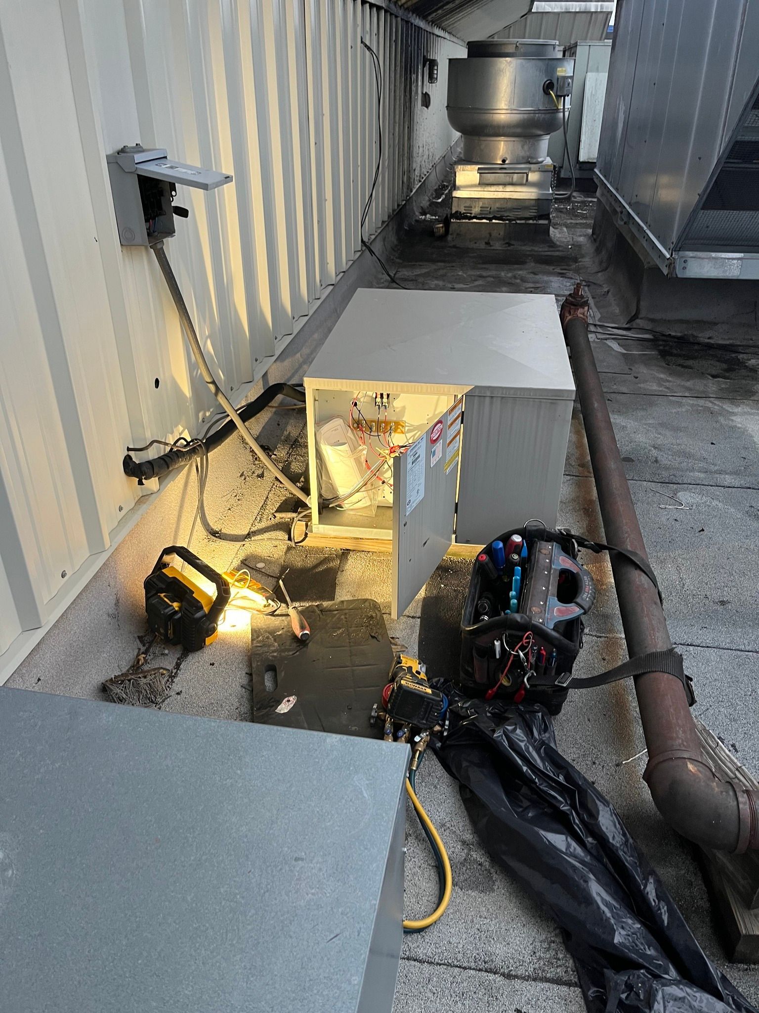 HVAC equipment on a rooftop, with open electrical panel and tools. Gray and metallic tones, exterior.