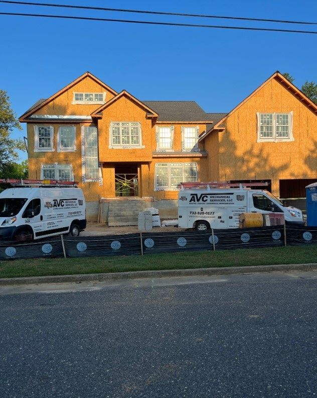 New house construction site with two JVC vans in front. Blue sky, wooden framing.