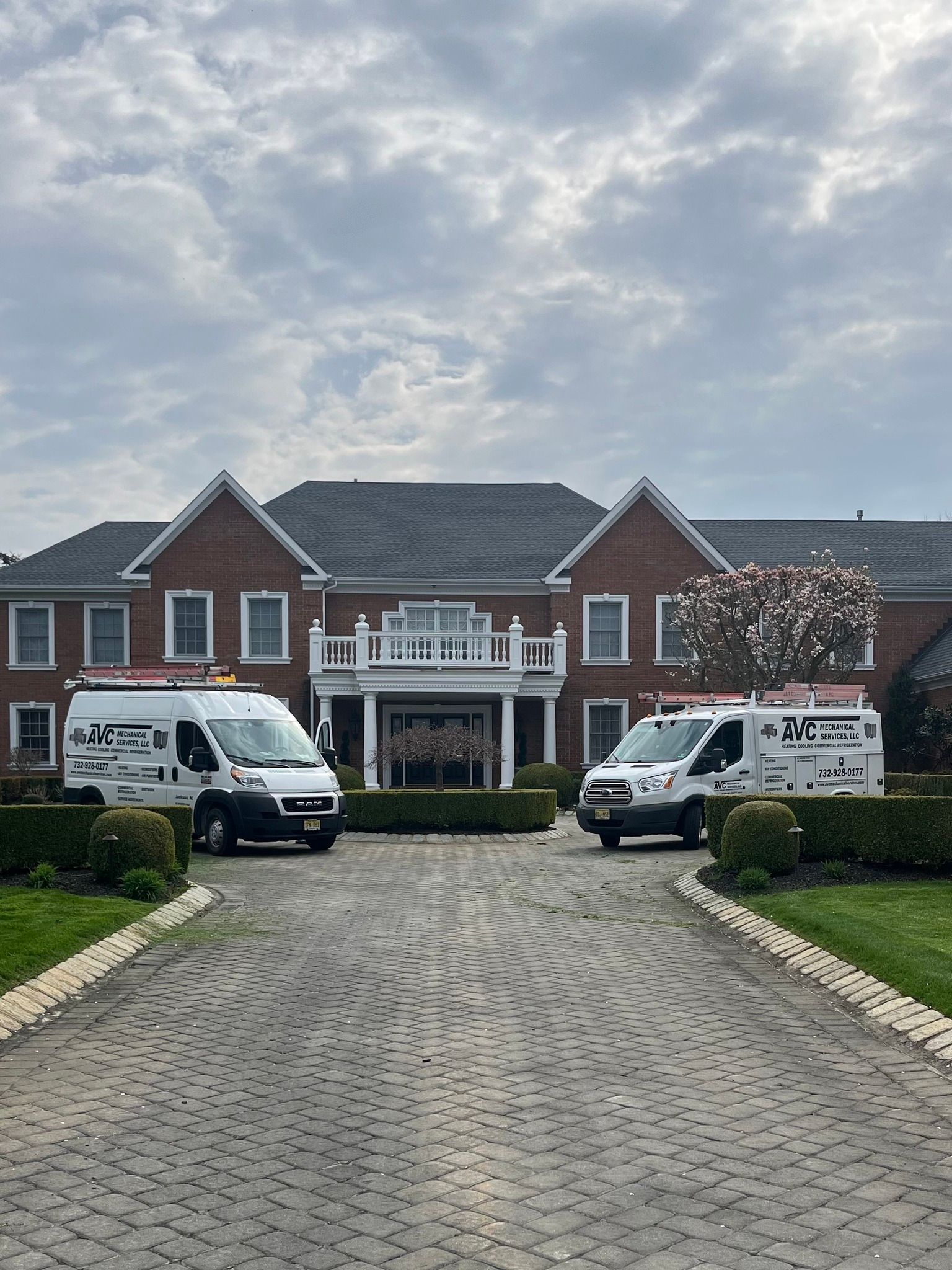 Two service vans parked in front of a large brick house. Cloudy sky.