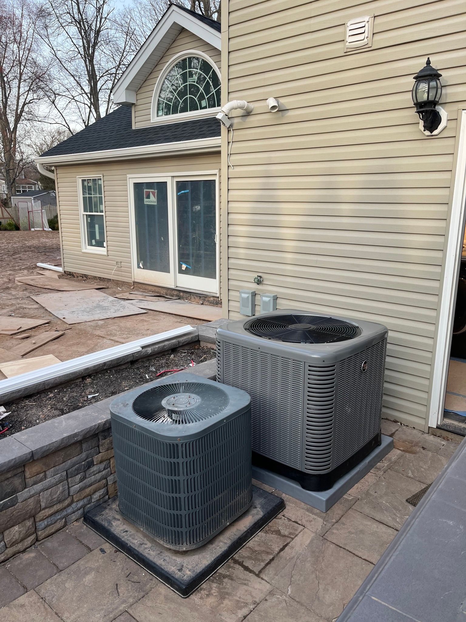 Two air conditioning units outside a house with tan siding.