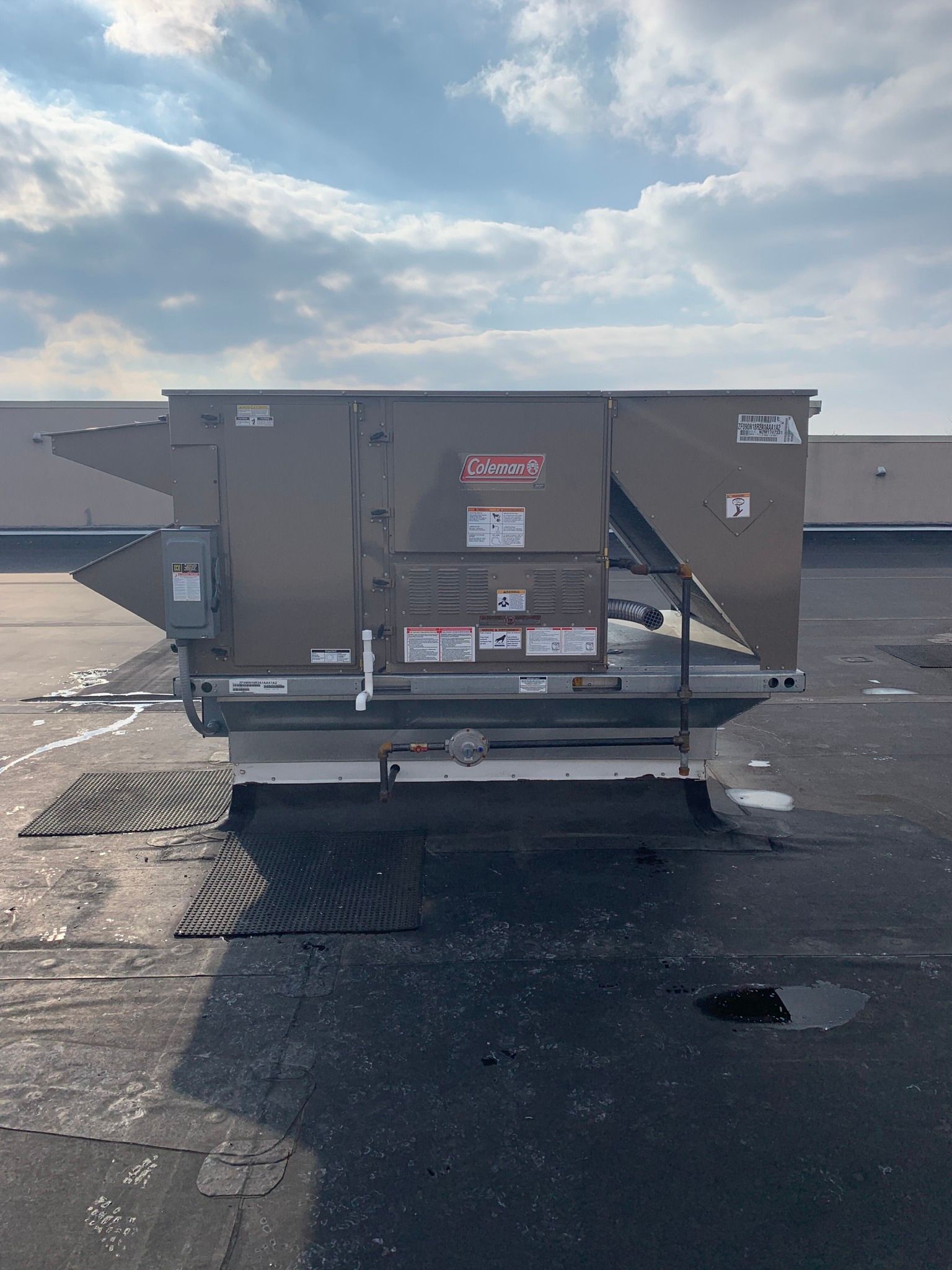 Rooftop HVAC unit, Coleman brand, on a flat, dark roof under a cloudy sky.