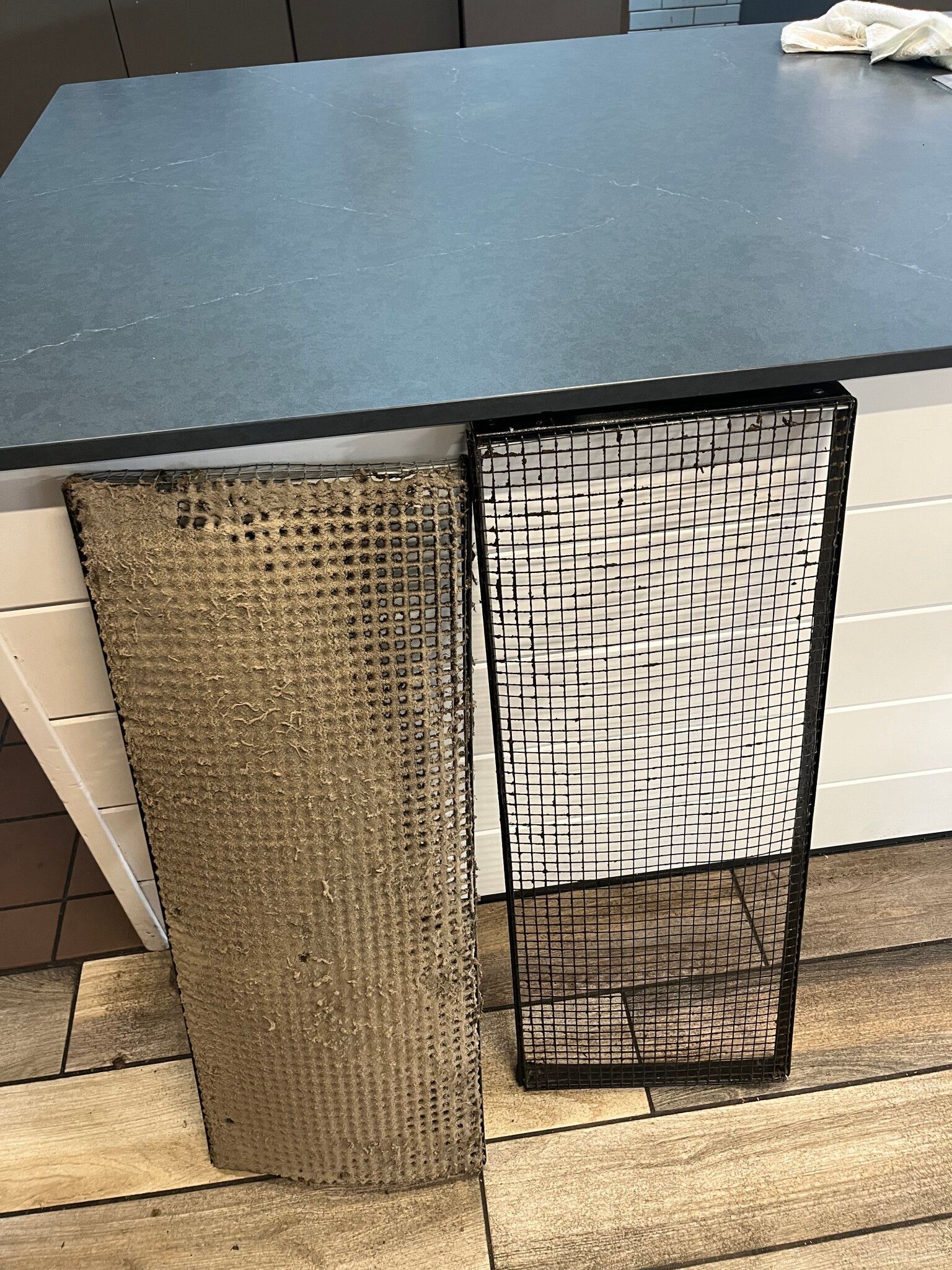 Two rectangular grill grates, one dirty and one clean, next to a kitchen island.