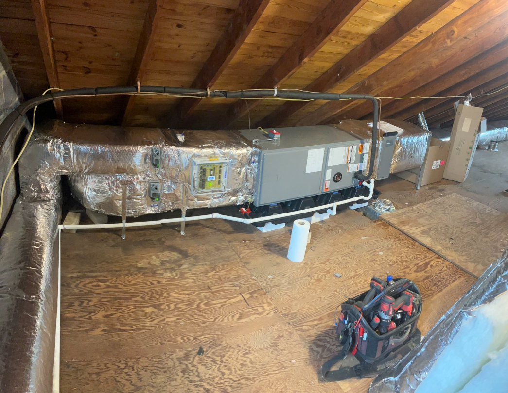 HVAC system in an attic with ductwork, a toolbox, and wood beams.