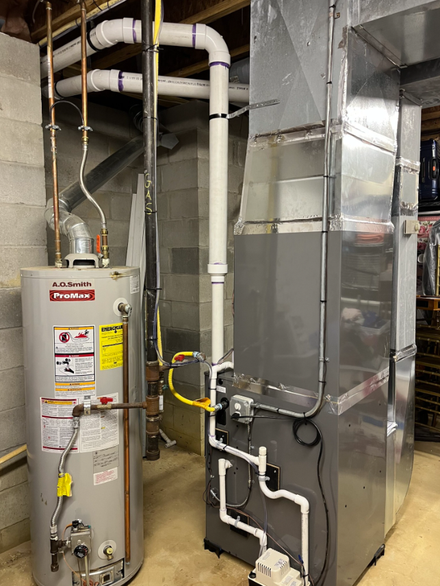Water heater and furnace in a basement. Gray and white pipes, gray furnace, silver water heater.
