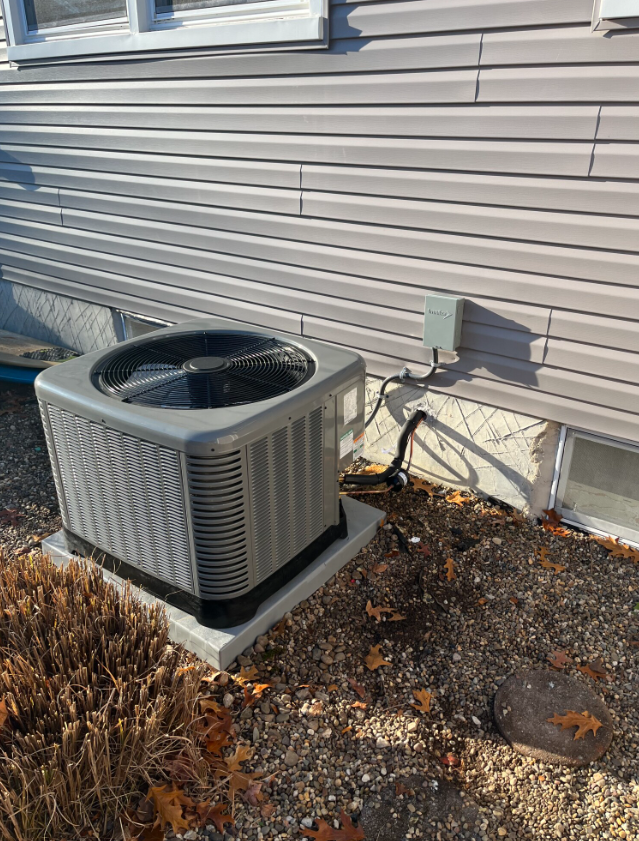 Air conditioner unit outside a house with gray siding on a concrete base, on gravel ground.