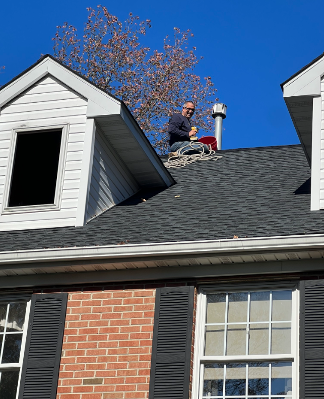 Man on a roof clearing leaves from around a chimney on a sunny day.