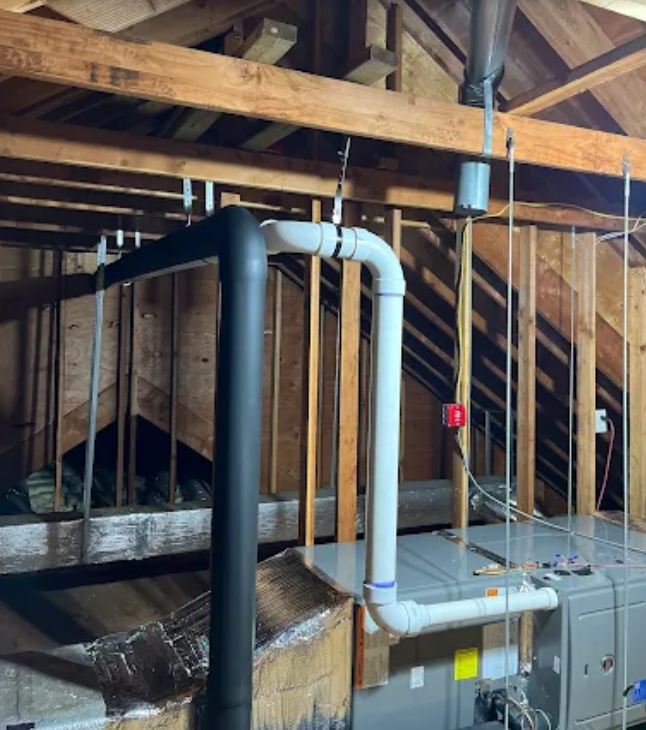 HVAC system in attic with black and white pipes. Wooden beams and framing visible.