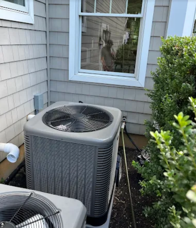 An outdoor air conditioning unit next to a house, next to some shrubs.
