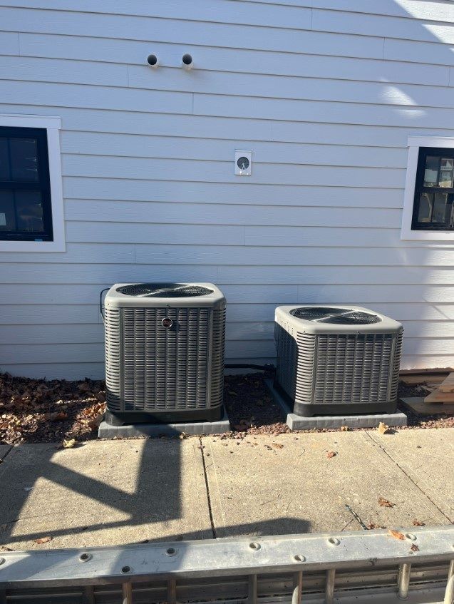 Two air conditioning units sit on concrete pads next to a white-sided building.