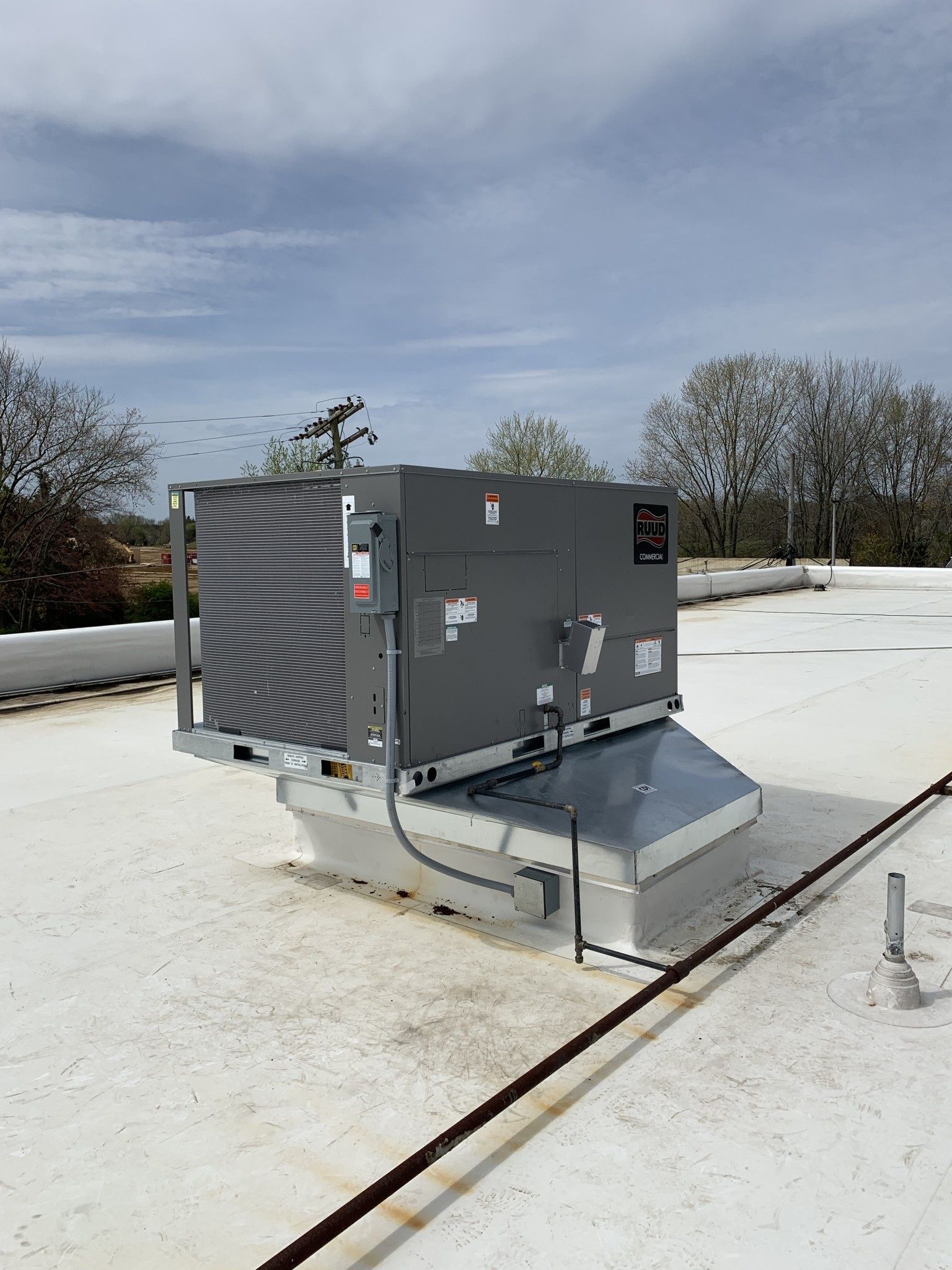 Rooftop HVAC unit on a white roof under a partly cloudy sky.