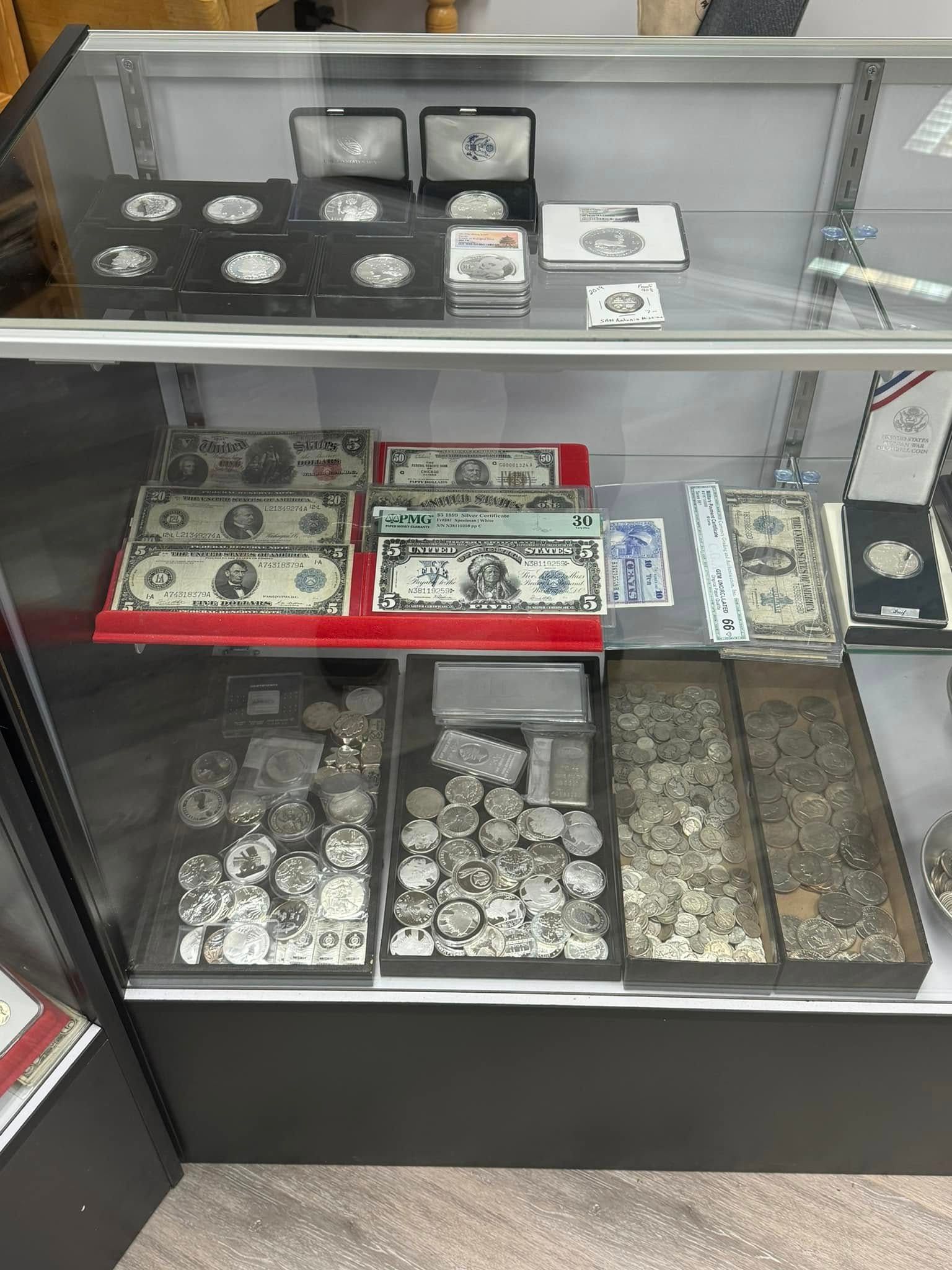 Glass display case with coins, currency, and silver bars in trays