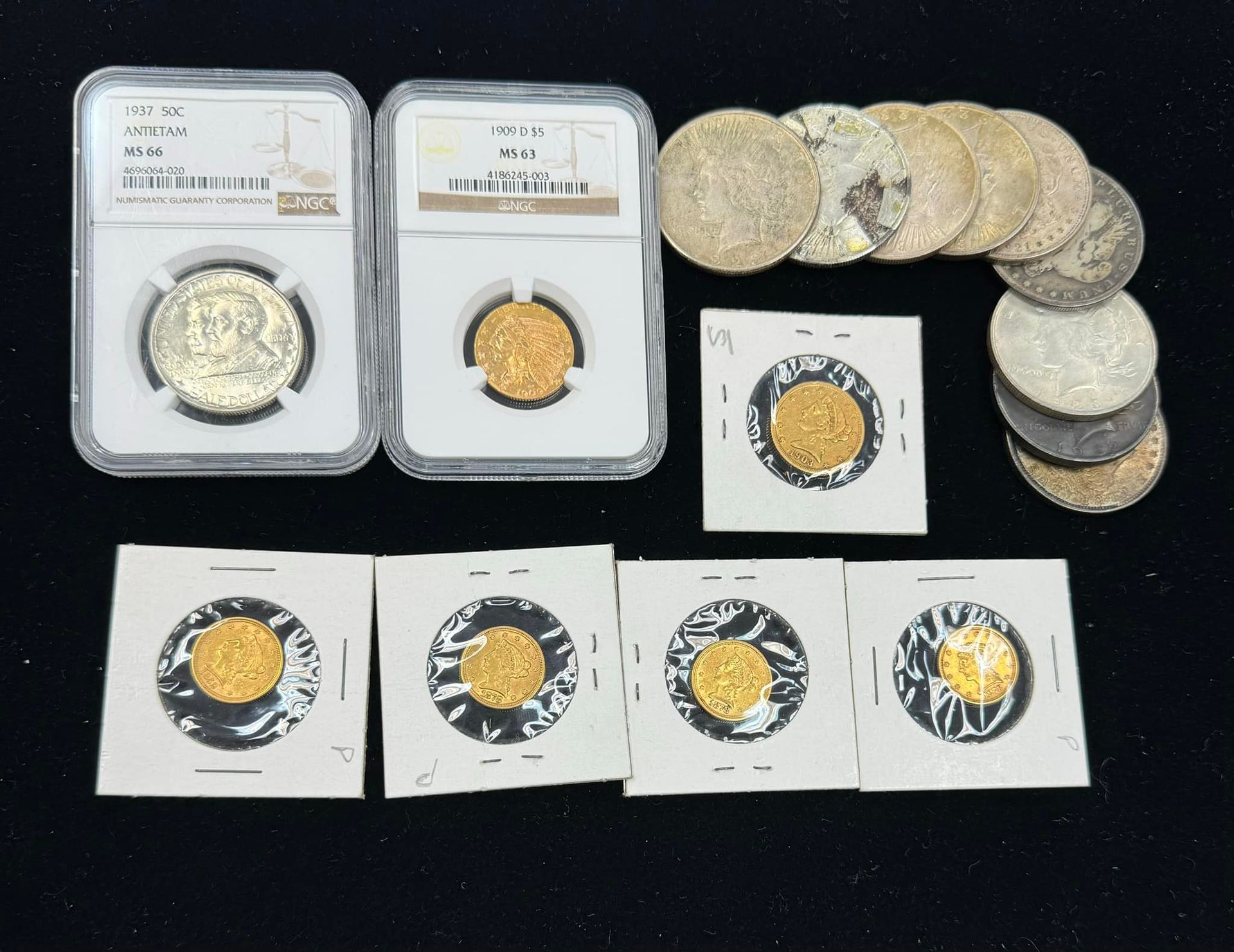 Assorted coins in plastic holders and sleeves arranged on a dark surface.
