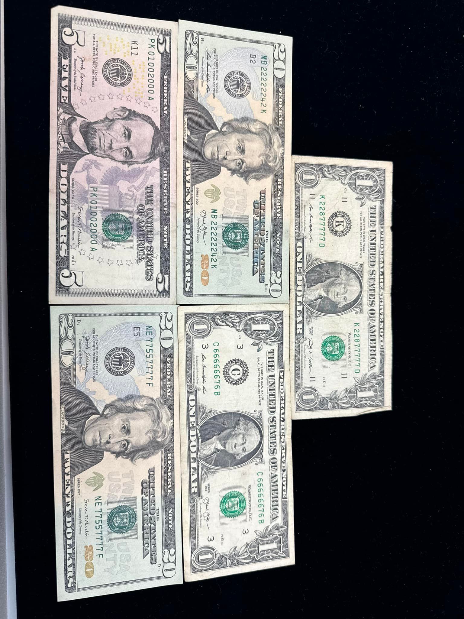 Four U.S. dollar bills arranged on a dark surface.
