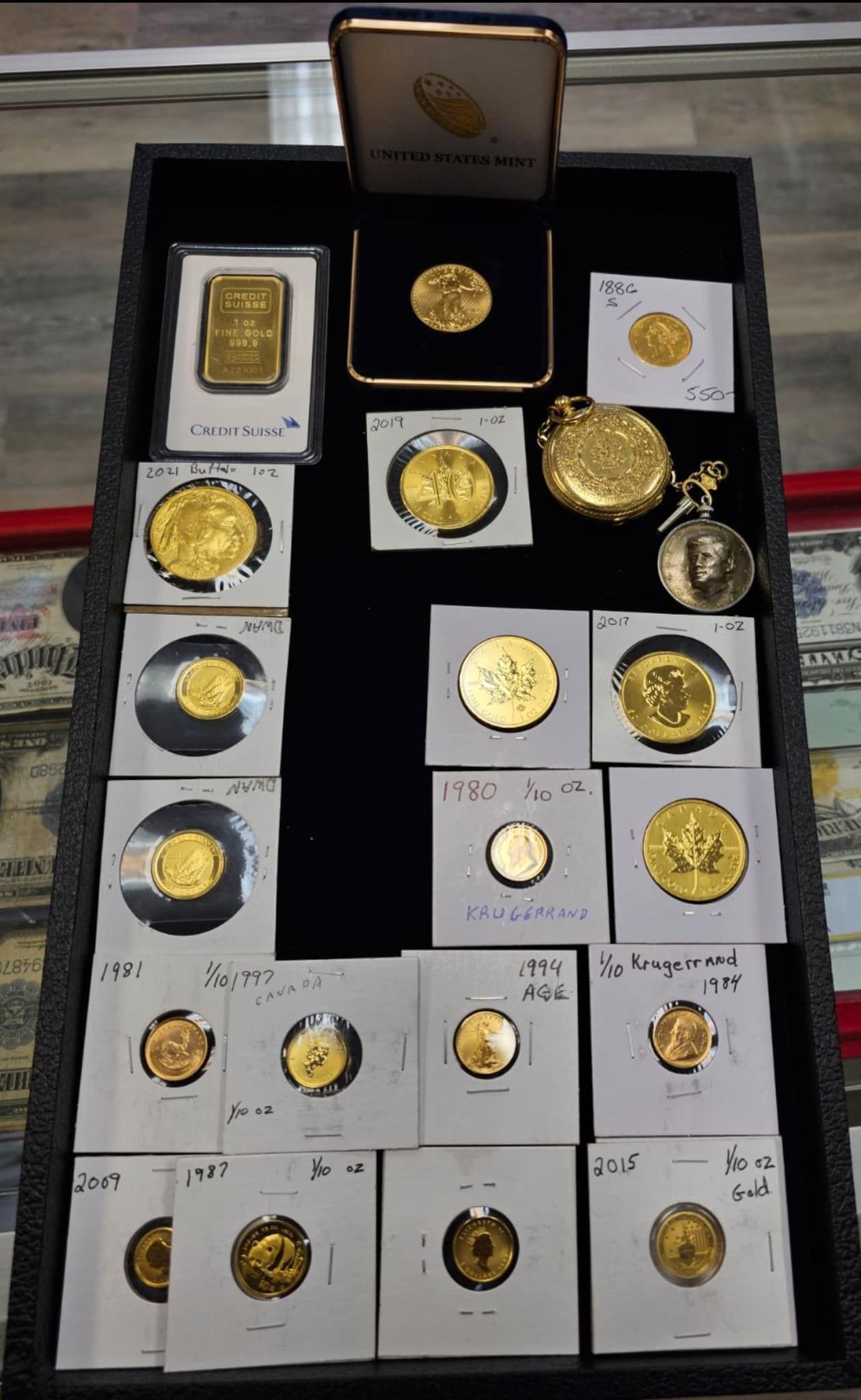 Gold coins and medallions arranged in a display case with white cards and black backing.