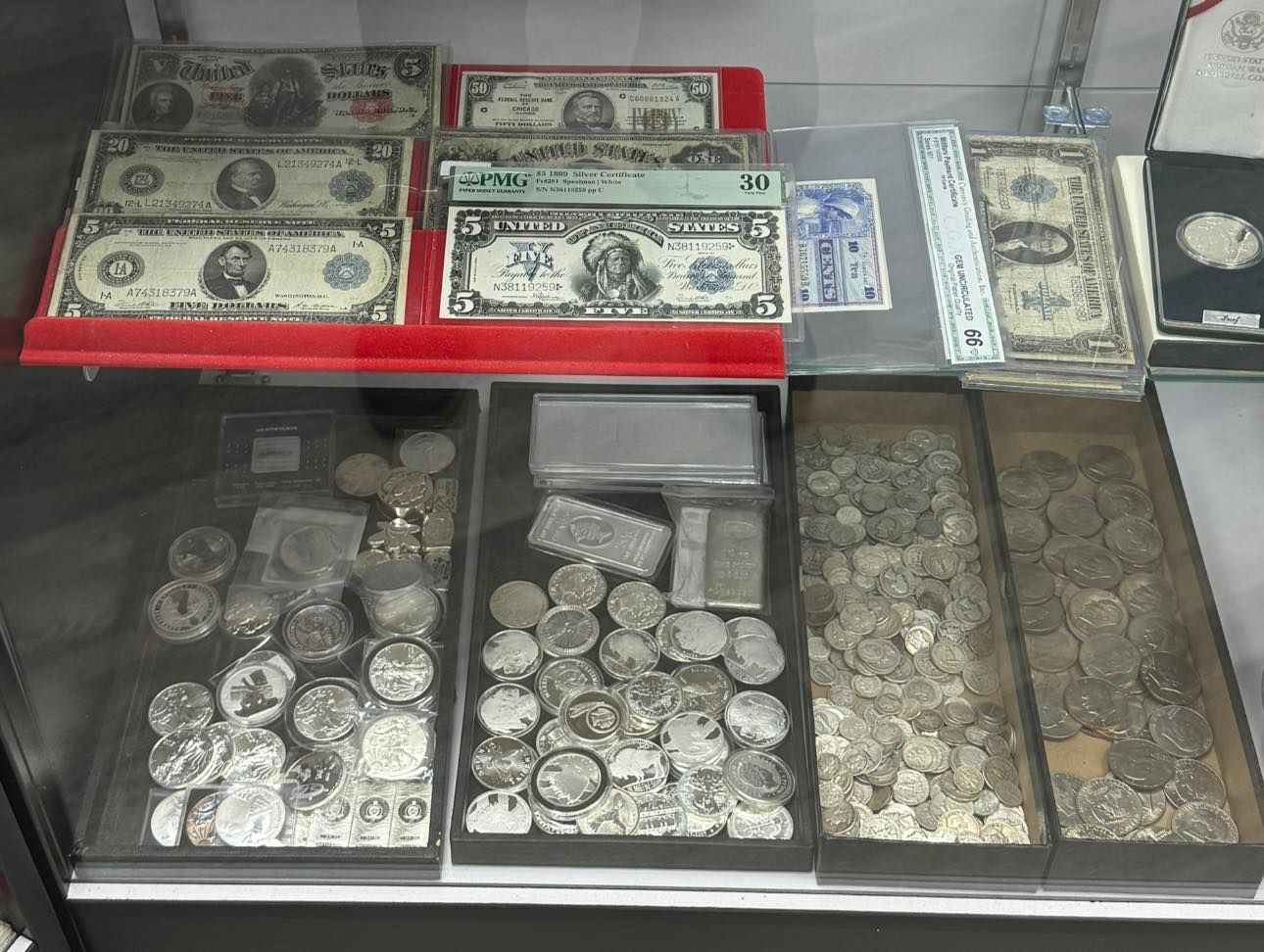 Tray of assorted old coins and banknotes displayed in a glass case.