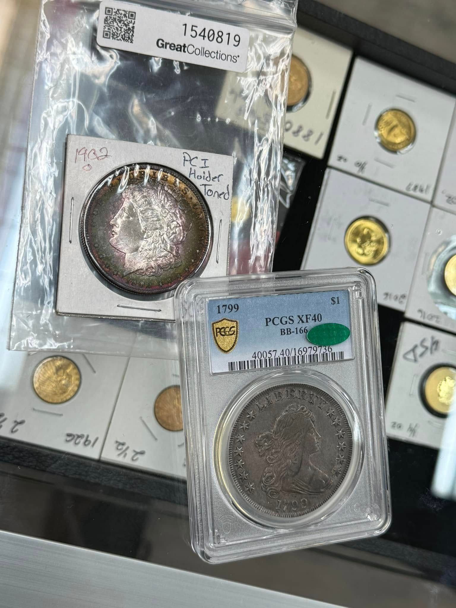 Graded coins in plastic holders on a black surface, with two coin slabs in the foreground.