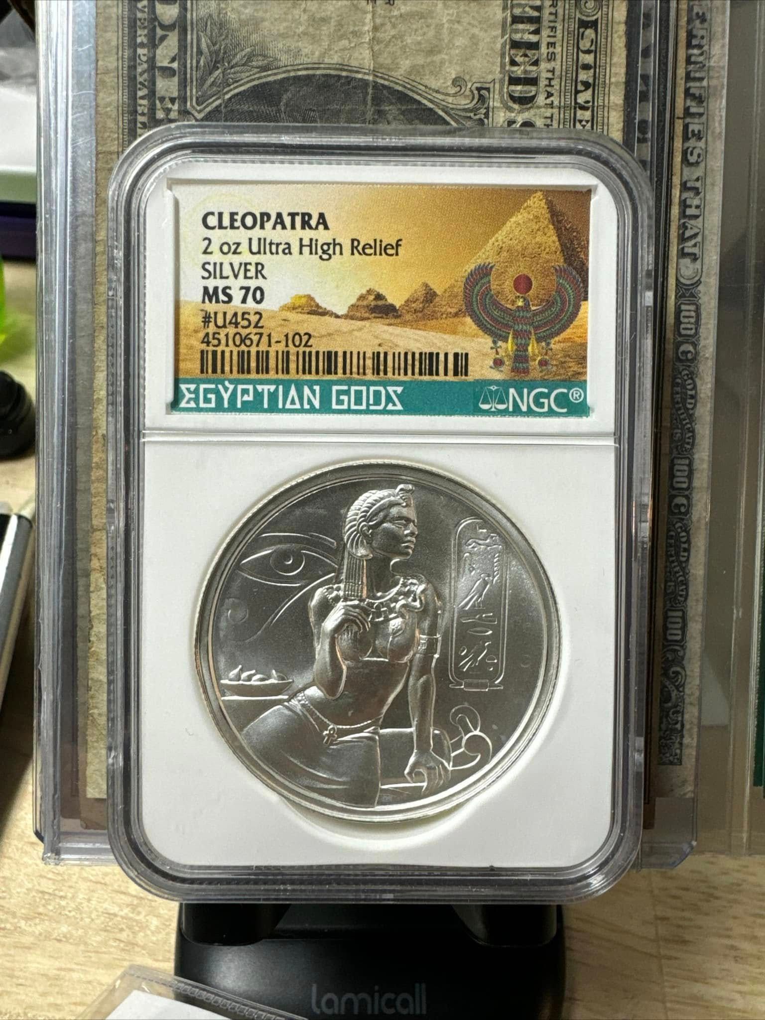 Silver Cleopatra coin in graded case with gold label, displayed upright on a stand.