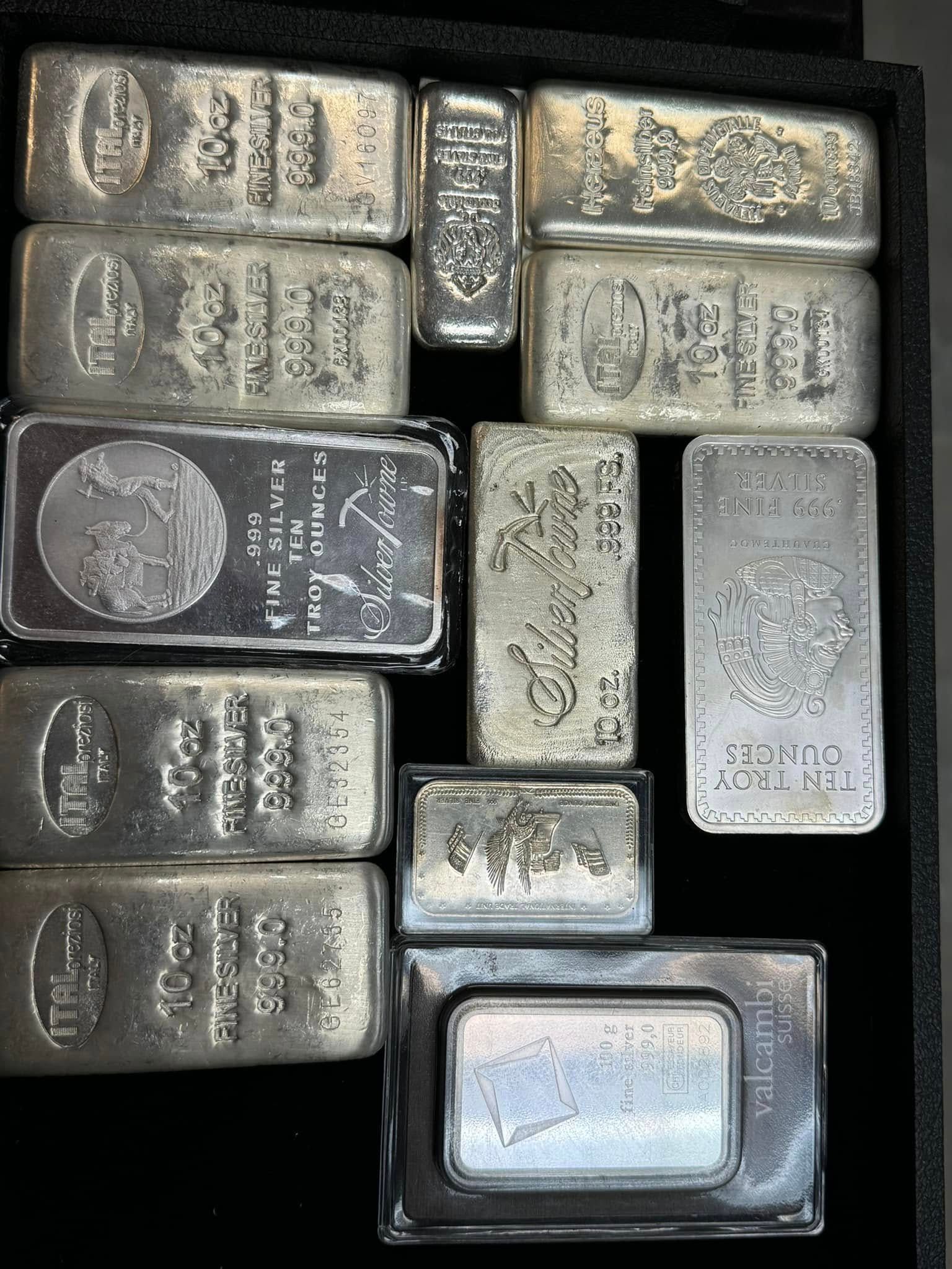 Assorted small silver metal bars and ingots arranged in a tight cluster on a dark surface.
