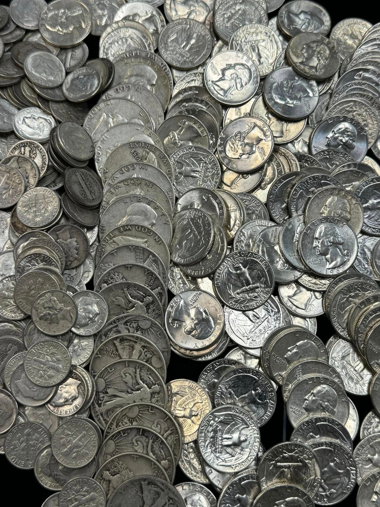 Piles of stacked silver coins filling the frame, with worn and shiny surfaces mixed together