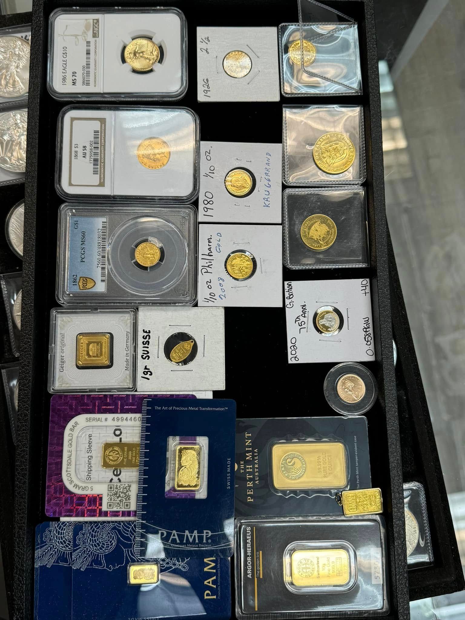 Assorted gold bars and coins in display cases and packaging on a dark surface
