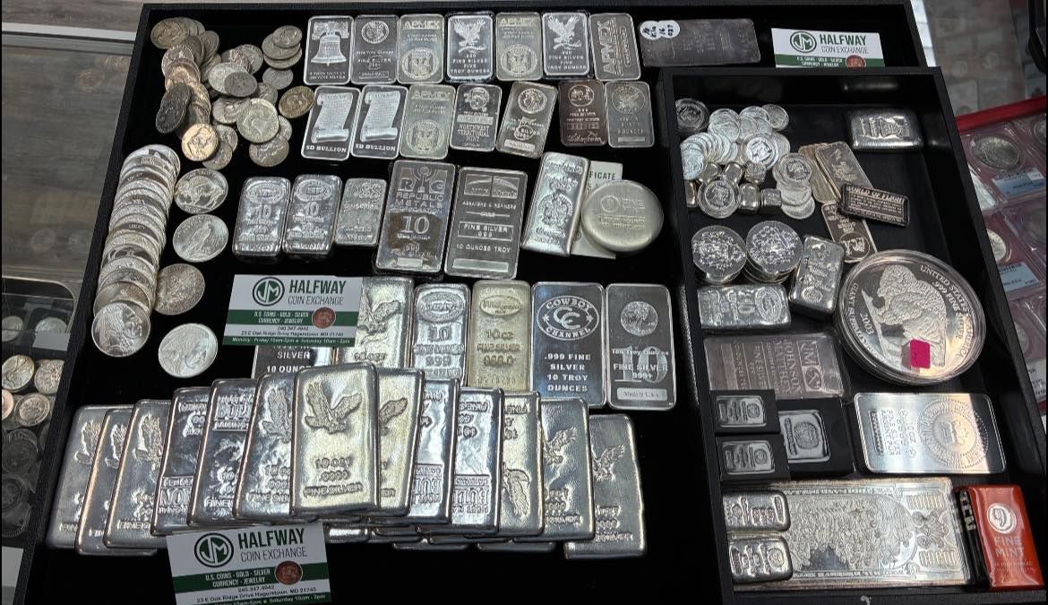 Tray of assorted silver bars and coins arranged in a display case, with some gold-colored items.