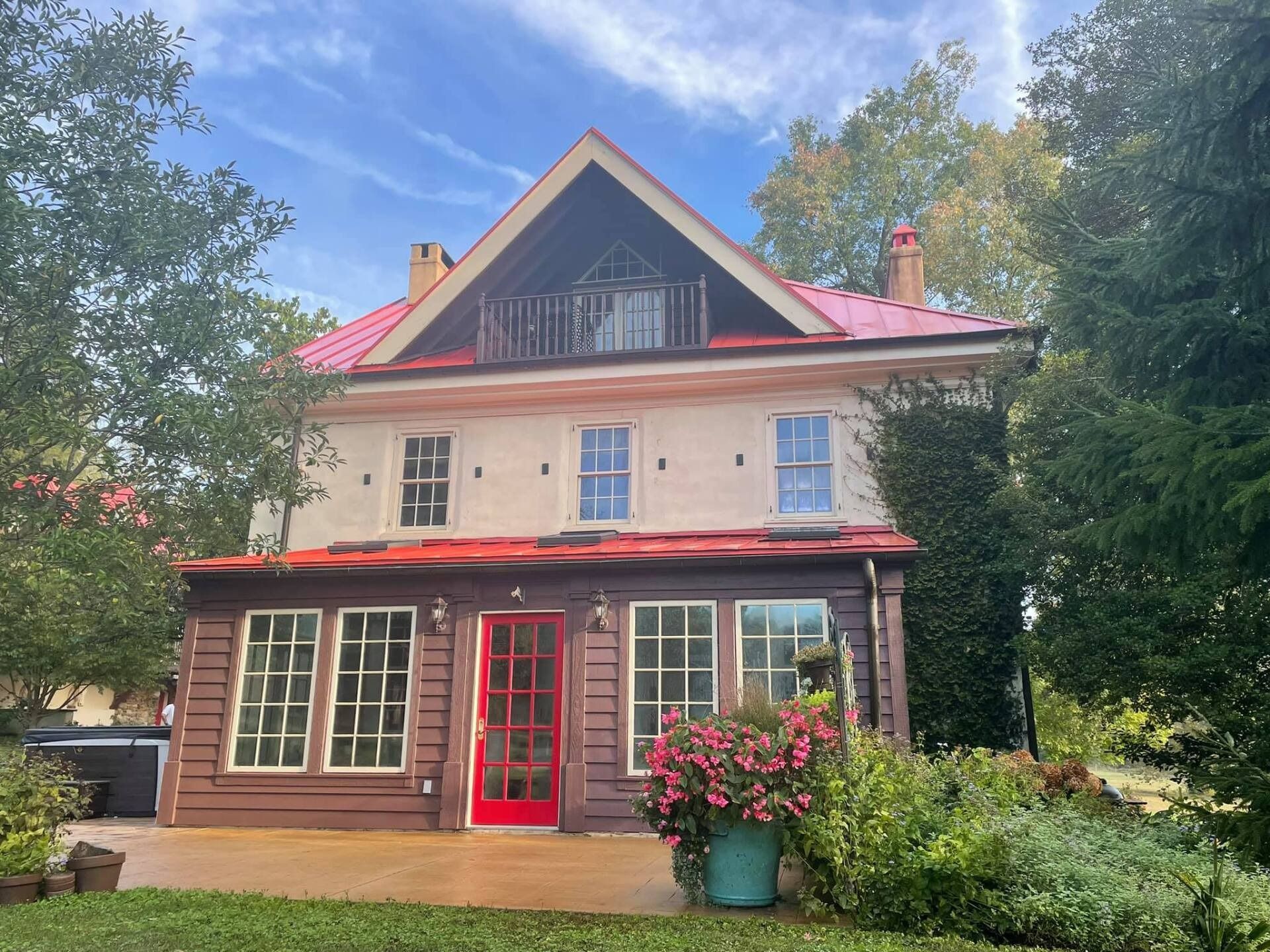 Two-story house with red roof, porch, and a red front door. Beige siding, green foliage, and blue sky.