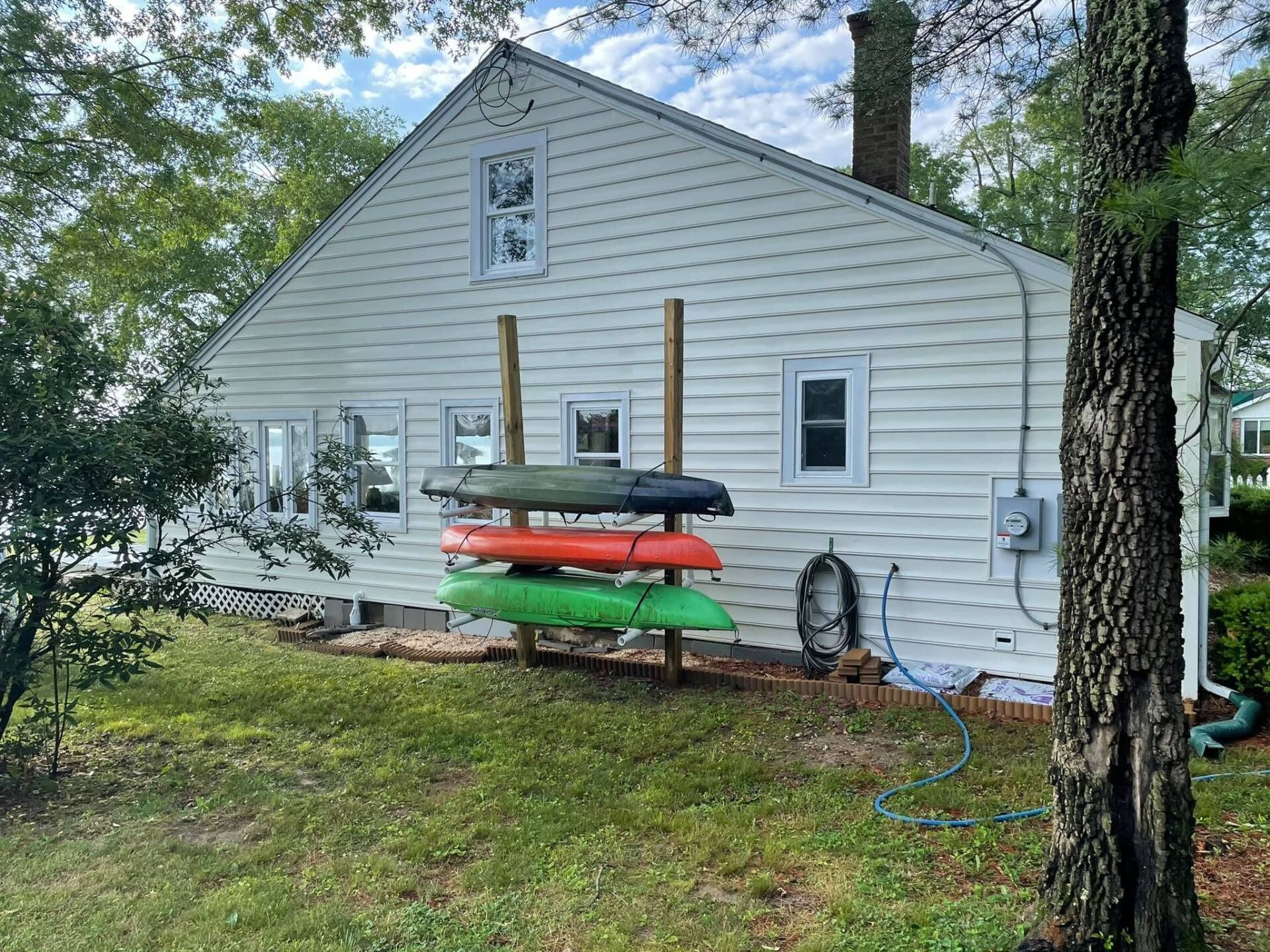 Side of a white house with a kayak rack holding three kayaks in green, red, and black.