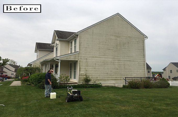 Before photo of a beige two-story house with people and equipment on the lawn
