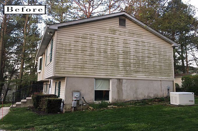 Before photo of a tan two-story house with a sloped roof and basement, viewed from the yard.
