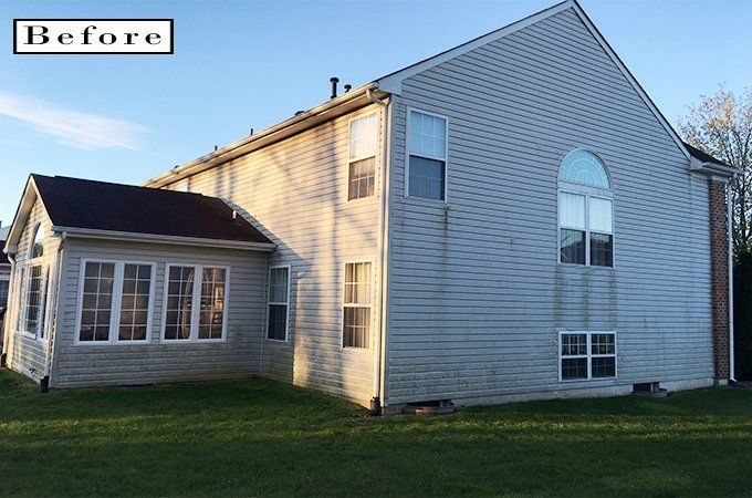 Before photo of a gray two-story house with an attached sunroom, shown in evening light