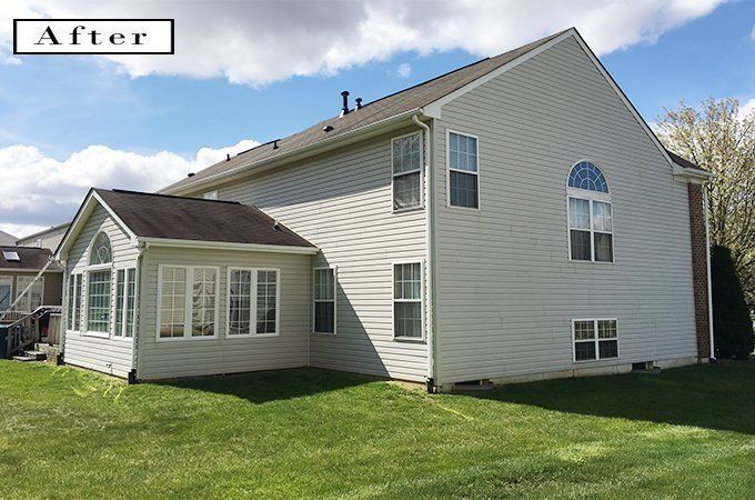 Side view of a white house with beige siding and a sunroom on a grassy lawn under a blue sky
