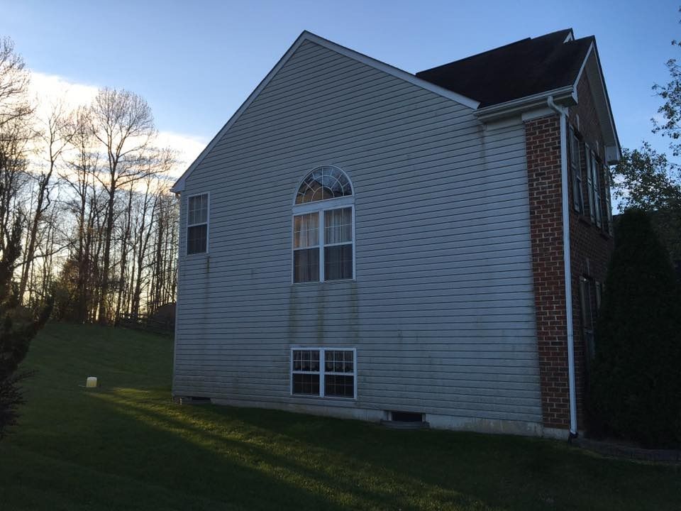 White house with a gabled roof beside a grassy yard at sunset, trees in the background
