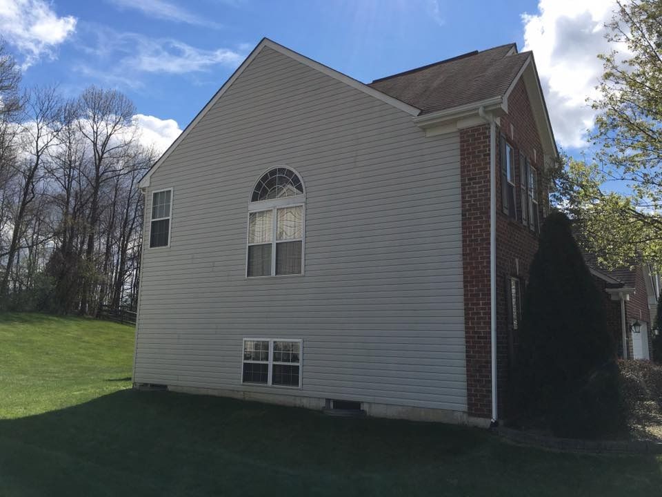 Side view of a beige house with brick accents, grassy yard, and trees under a partly cloudy sky